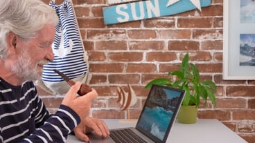 Senior man smoking pipe using laptop to see photographs of the sea. Brick wall in the background and decorations