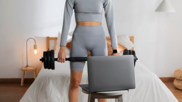 Female fitness instructor lifting weights at home in front of laptop