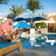 Young man, relaxing on sun loungers by the pool, texts on his phone.