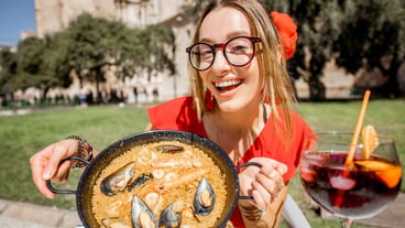 Young woman in a red dress with seafood paella, a traditional Valencian rice dish, sitting outside a restaurant in the center of Valencia's old town