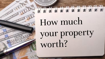 Banknotespencompass and notebook written with text How much your property worth on wooden background
