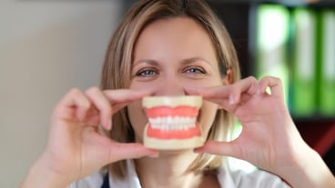 El dentista sostiene la mandíbula con dientes artificiales frente a la boca, estomatología y atención dental.