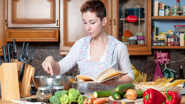 beautiful woman cooking vegetables with cookbook