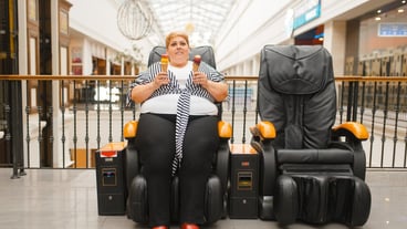 Fat woman with ice cream sitting in a massage chair in mall. Overweight female person poses in a leather armchair in shopping center, obesity problem