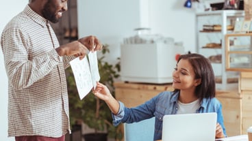 Best option. Charming cheerful young man showing two printouts with project design concepts and the woman choosing one of them