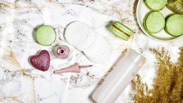 Cotton pads and nail polish with macarons and daisies, reeds and micellar water on marble backing