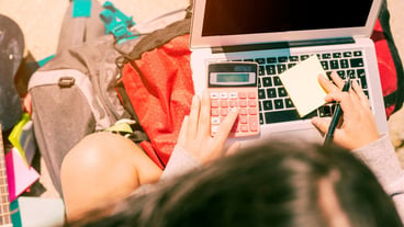 Woman taking notes by hand with calculator on laptop on sunny day