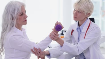 Physiotherapist helps old woman to do recovery exercise with dumbbell for injured hand in