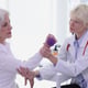 Physiotherapist helps old woman to do recovery exercise with dumbbell for injured hand in