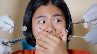 Girl frightened by dentist covers her mouth at dental clinic