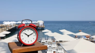 Red alarm clock stands against background of the beach and sea summer time vacation concept