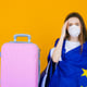 Beautiful girl in a white summer dress with a suitcase Medical mask on the face Closed borders