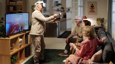 Group of cheerful senior friends looking at mature man with gamepads