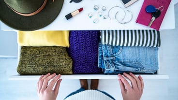 Woman choosing outfit from drawer dresser with stylish casual trendy clothes, home stuff and female accessories. Top view.
