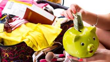 Girls hand holds piggy bank passport on open suitcase expenses for vacation dollar bill and money box