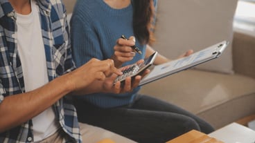 Two Asian bloggers show off their outfits in front of the camera to record a live video stream from their online shopping cart, apparently from their couch at home.