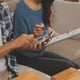 Two Asian bloggers show off their outfits in front of the camera to record a live video stream from their online shopping cart, apparently from their couch at home.