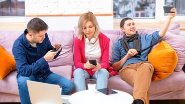 Friends are sitting on the couch chatting and using a smartphone desktop laptop