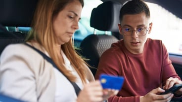 Man and woman mother and son using smart phone and credit card sitting in car on the street