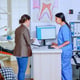 Young lady asking informations filling in stomatological form while patients talking sitting on chair in waiting area. People speaking in crowded professional orthodontist reception office.