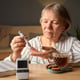 A senior woman is measuring her blood sugar levels with a glucometer at a wooden table Next to her a cup of tea and a plate of cookies sit creating a warm atmosphere