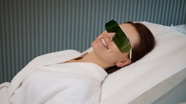Charming pleased middle aged woman in protective UV goggles lying on a medical massage couch in spa salon and smiles with beautiful toothy smile enjoying wellness procedures Cosmetology concept