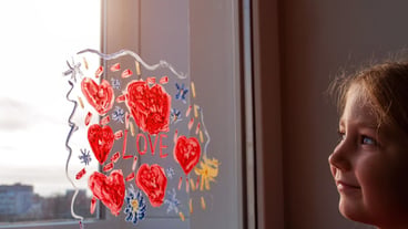 Little girl holds paintbrush in hand drawing red heart on window glass Valentine's day love dating quarantine leisure