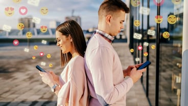 Young couple standing back to back at rooftop and using smart phones for social media