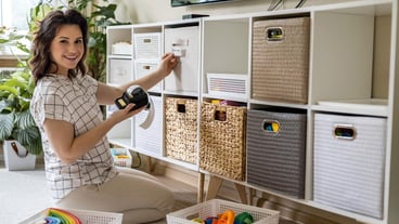 Smiling woman applying printed paper sticker on title inscription for children's toy storage and home organization