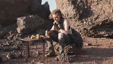 Homeless young woman sitting on a rock and eating potatoes outdoors