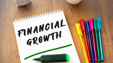 A notebook on a spring with the text FINANCIAL GROWTH lies on a brown wooden table.