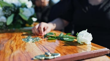 Coffin flower and hand at memorial with respect grief or loss at family service for burial Person mourning and grieving relative with white rose on casket for remembrance at funeral at graveyard