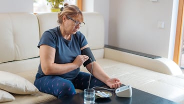 Senior woman checking blood pressure level at home older female suffering from high blood pressure sitting at a couch and using a pulsometer tonometer