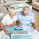 Senior couple smiling checking utility bills or insurance at computer with easy access elderly users of technology
