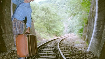 Side view of a child holding luggage while standing on the railroad track.