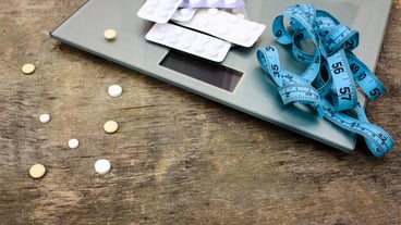 Measuring tape, pills and scales on wooden background.