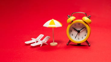 Time to travel. Sun lounger, umbrella and alarm clock on a red background.