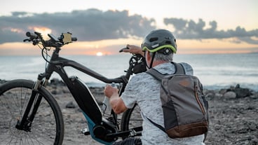 Rear view of active caucasian senior man with electric bicycle at sunset on the beach elderly man with helmet enjoying healthy lifestyle
