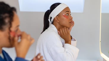 Happy biracial lesbian couple in bathrobes wearing eye masks in bathroom. Lifestyle, beauty, self care, wellbeing, relationship, togetherness and domestic life, unaltered.