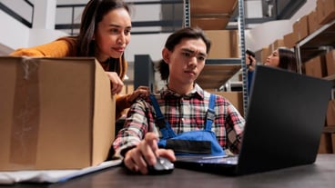 Warehouse shipment managers reading delivery customer satisfaction on laptop. Retail storehouse asian man and woman employees checking pick ticket and preparing box for dispatching