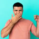 Handsome young man holding a Bitcoin against an isolated blue wall, happy and smiling, covering his mouth with his hand