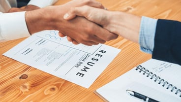 Two happy businessmen shake hands over resume papers Entity