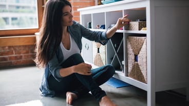 Woman sitting next to a shelf indoors
