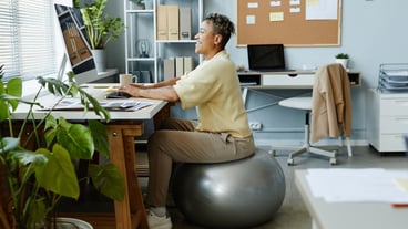 Side view portrait of black young woman sitting on fitness ball at workplace and smiling sports acti