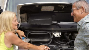 An older couple laugh happy in front of a car engine