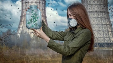 Side view of woman in gas mask holding plant in container while standing against industry
