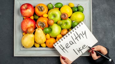 Top view of handwriting healthy life on spiral notebook on collection of fresh fruits in photo frame on dark background