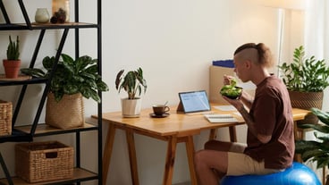 Project manager sitting on fitness ball eating salad and checking mockups sent by ui designr
