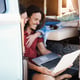 Happy couple using laptop computer inside minivan during road trip vacation - Focus on man face