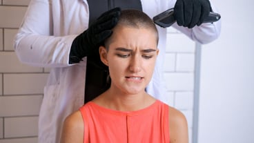 Young woman is forcibly shaving her head with an electric razor holding